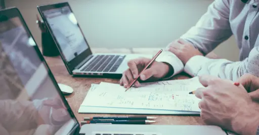 person holding pencil near laptop computer